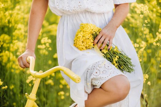 a woman enjoys a bike ride through a field full of bright yellow rapeseed with a bouquet in her hands.