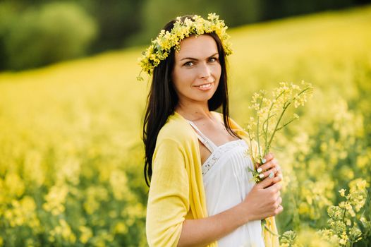 a woman with a yellow bouquet in her hands and a wreath on her head stands in a meadow.