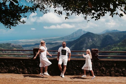 a happy family, a man, a woman and a daughter, are jumping merrily against the background of mountains and jungles of the island of Mauritius.A couple and daughter in the jungle of the island of Mauritius in white clothes walking in Africa