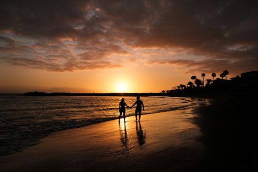 Romantic couple on the beach in a colorful sunset in the background.A guy and a girl at sunset on the island of Tenerife.