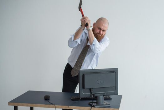 Stressed crazy businessman smashing his computer in office using ax problem concept. The man has problems at work and frustration