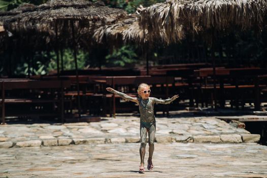 A cute little girl kid is laughing as she plays outside in the mud. Child is showing her dirty hands