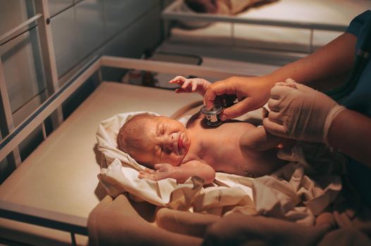 Doctor paediatrician examining baby in clinic, newborn baby crying in bed.