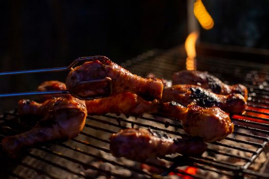 chicken drumsticks are grilled on a barbecue grill in the evening