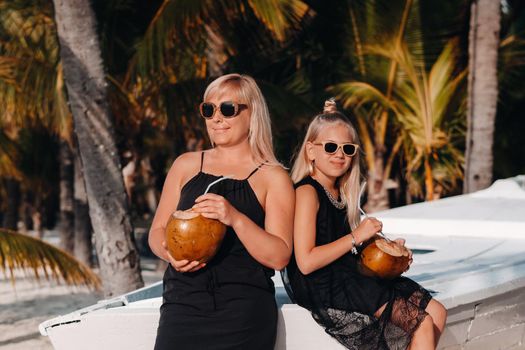 a stylish family in black clothes with coconuts in their hands on the beach of the island of Mauritius.Beautiful family mother and daughter on the island of Mauritius in the Indian ocean.