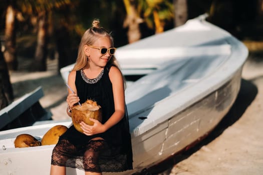 Cute little girl on the beach with coconut while relaxing.A girl on the beach near a boat with a coconut.Mauritius island.