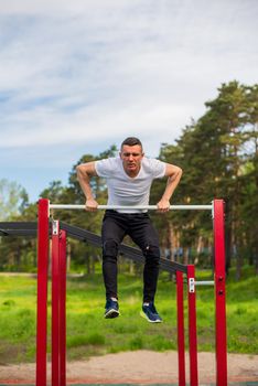Caucasian man pulls himself up on a horizontal bar on a sports ground