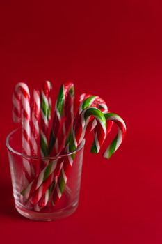 Christmas candies in the form of a cane stand in a transparent glass glass on a red background. Vertical orientation of the image. Christmas lollipops.