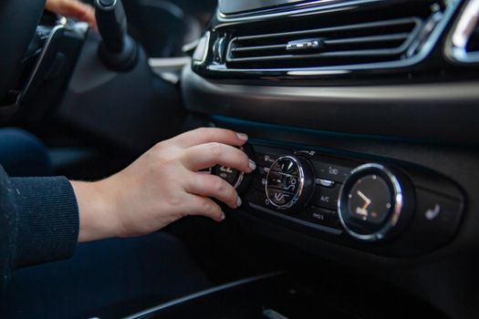 Woman's hand switches the air conditioning in the car. Driver turning on car air conditioning system. moderm climate control system in modern premium car