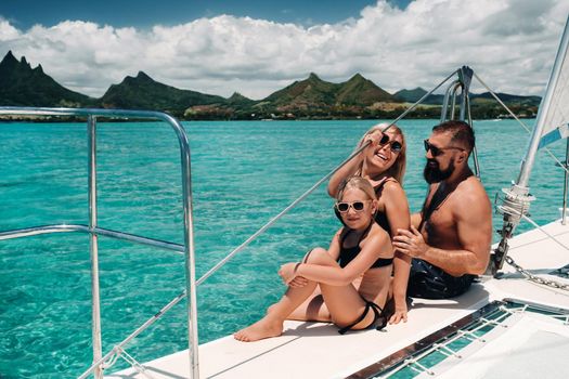 a happy family in swimsuits sits on a catamaran in the Indian ocean. portrait of a family on a yacht in the coral reef of the island of Mauritius