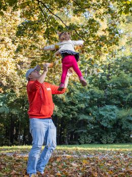 dad and child are playing in the park. dad tosses Toddler's daughter.