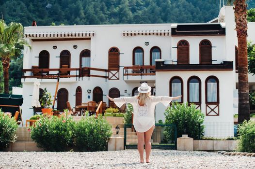 A beautiful girl in a tunic and hat stands near a Villa with a beautiful view.A woman enjoys a holiday in a Turkish resort.