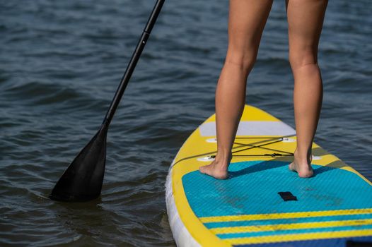 Caucasian woman swims on a SUP board. Close-up of female legs on the surf