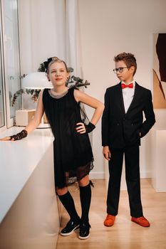 Stylish and elegant boy and girl stand at the window in the interior of the house.