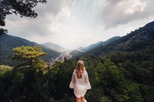 A girl in white stands back and looks at the expanses of the gorge in the mountains, a Woman in the mountains of Turkey enjoys nature.