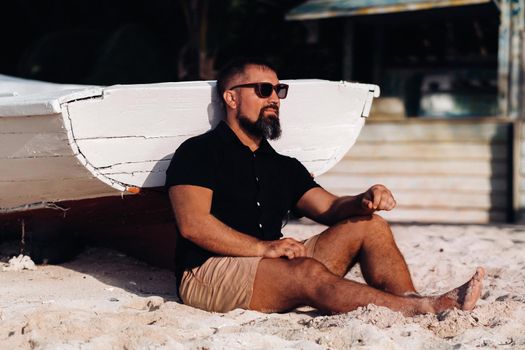 Portrait of a beautiful brutal man, enjoying and relaxing, sitting on the beach of the island of Mauritius.The man on the beach of Le Morne in the black clothes and glasses. tropical beach.