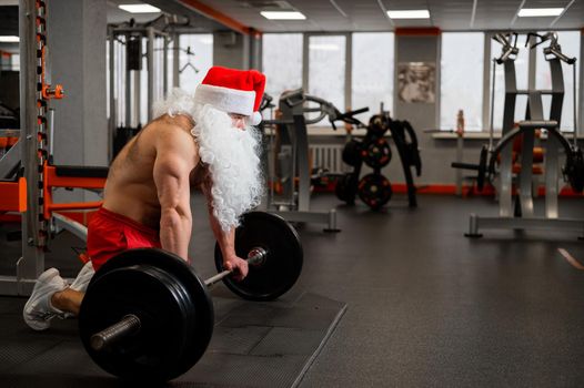 Santa claus in the gym. Muscular man with a naked torso doing exercises with dumbbells