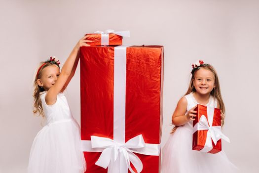 two little girls with Christmas gifts on a white background and a huge gift.