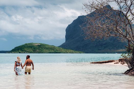 A girl in a swimsuit and a man in shorts stand in the ocean against the backdrop of mount Le Morne on the island of Mauritius.A couple in the water look into the distance of the ocean against the background of mount Le Morne .