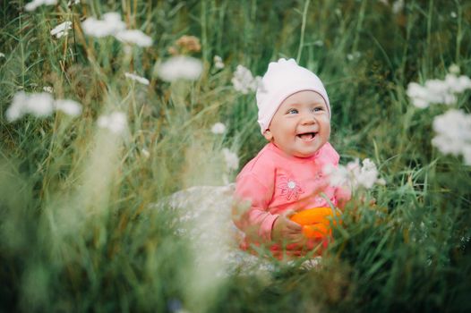 Beautiful happy little girl sitting on a green meadow with white flowers in nature in the Park.