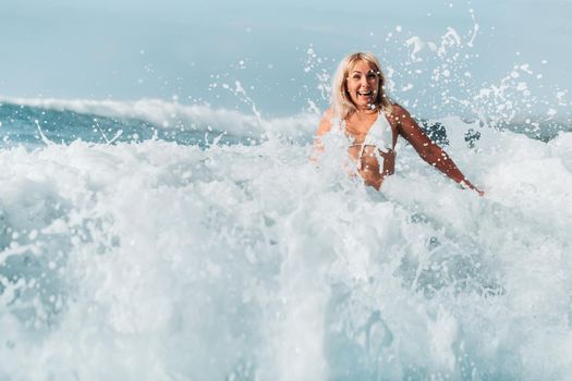 A girl with wet hair jumps over large waves in the Atlantic ocean, around a wave with splashes of spray and water drops.Tenerife.Spain.