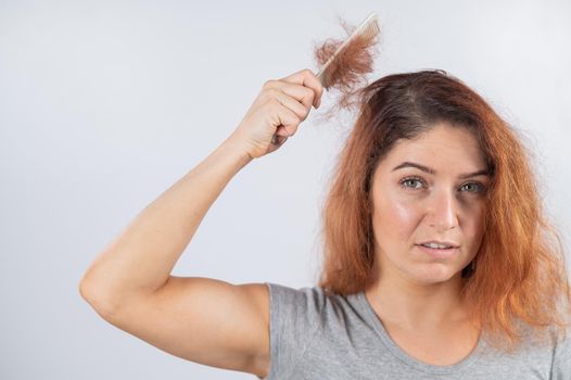 Caucasian woman with a grimace of horror holds a comb with a bun of hair. Hair loss and female alopecia