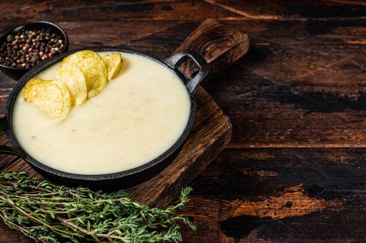 Potato cream soup with potato chips in pan on wooden board. Dark wooden background. Top view. Copy space.