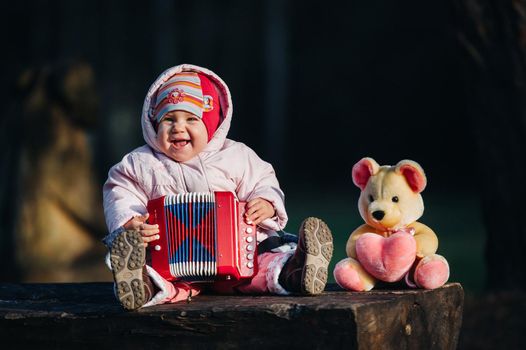 funny cute girl, a small child in fashionable jeans plays the accordion. Happy baby plays the game. Cute adorable baby. Beautiful expressive laugh of a smiling baby.