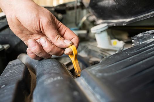 An auto mechanic pulls out a dipstick to check the oil level in a car engine