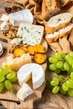 Assorted Cheese Brie, Camembert, Roquefort, parmesan, blue cream cheese with grape, fig, bread and nuts. wooden background. Top view.