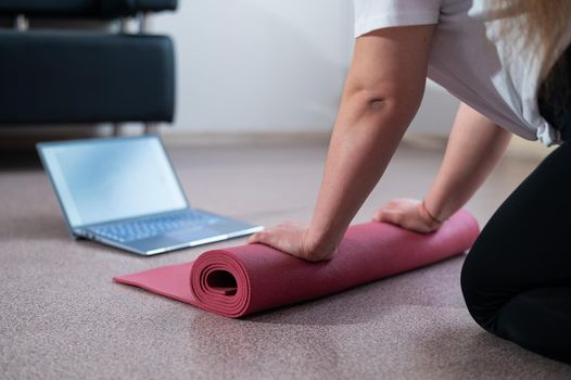 Young chubby woman folds sports mat after online fitness class.