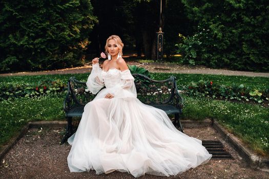 Bride's morning in the garden. Portrait of a young bride looking at her wedding dress, hanging on a garden tree