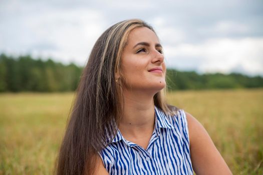 portrait of a beautiful swarthy caucasian young woman on a background of a field, nature. smiling happy young adult