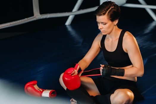 portrait of a female boxer with red gloves after training sitting in the ring.