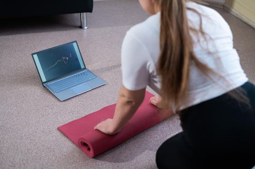 Young chubby woman folds sports mat after online fitness class.