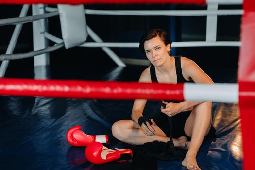 portrait of a female boxer with red gloves after training sitting in the ring.