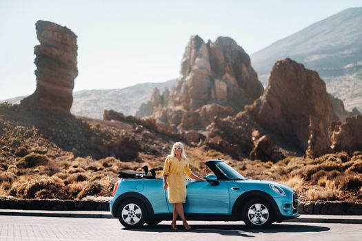 Girl in yellow dress enjoying a road trip in a convertible through a deserted valley with mountains, Canary Islands, Tenerife