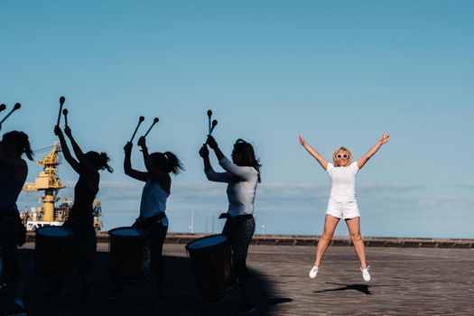 A girl in white clothes jumps up against the background of people doing fitness in the city of Santa Cruz de Tenerife on the waterfront. Canary Islands, Spain.