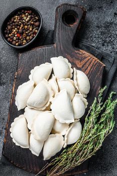 Frozen raw dumplings pierogi with potato on a wooden board. Black background. Top View.