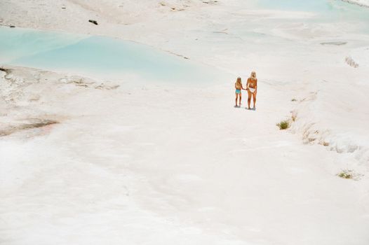 a little girl with her mother in bathing suits and sunglasses on a White mountain, a Family on a Sunny summer day on another planet, Pamukkale, Turkey.
