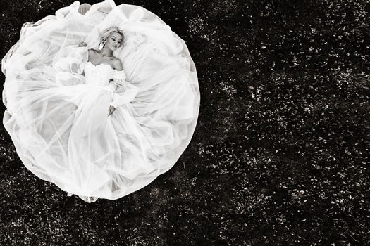 Portrait of a beautiful bride lying on the ground in a white wedding dress.photo of an elegant bride on the green grass.Top photo of the bride,black-white photo.