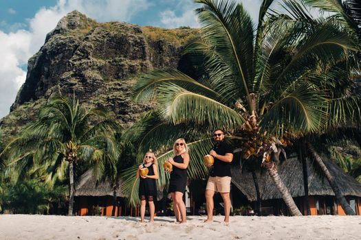 a stylish family in black clothes with coconuts in their hands on the beach of the island of Mauritius.Beautiful family on the island of Mauritius in the Indian ocean.