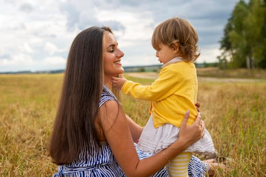Happy child and his mom have fun outdoors in a field flooded with . Mom holds the child in her arms, and the child hugs and kisses the mother. Mother's Day concept