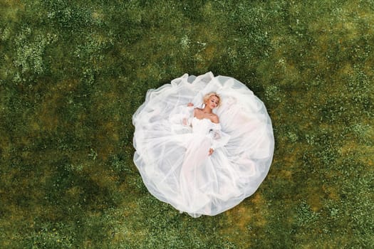 Portrait of a beautiful bride lying on the ground in a white wedding dress.photo of an elegant bride on the green grass.Top photo of the bride.