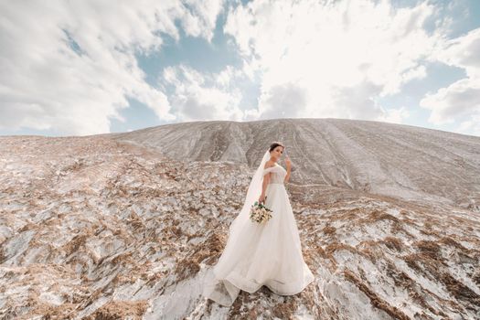 Beautiful bride in a wedding dress with a bouquet on the top of the salt mountains. A stunning young bride with curly hair . Wedding day. . Beautiful portrait of the bride without the groom