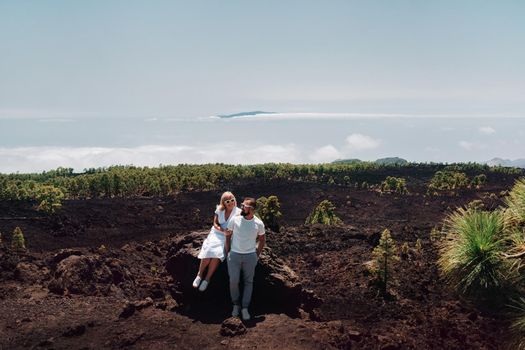 The family in white clothes are tourists traveling through the summer mountains of the Teide volcano in Tenerife. A young couple on a rocky mountain range looks at a beautiful view in the clouds and at the island of Gomera, Canary Islands.