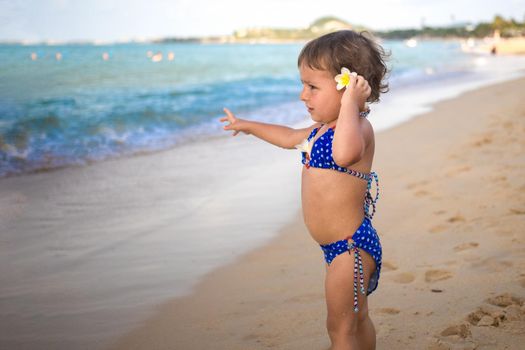 adorable toddler toddler stands on the sandy beach and points at the tropical sea