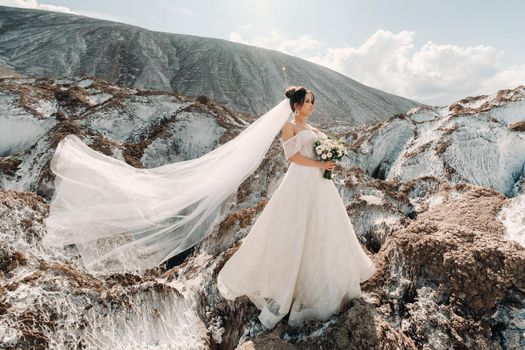 Beautiful bride in a wedding dress with a bouquet on the top of the salt mountains. A stunning young bride with curly hair . Wedding day. . Beautiful portrait of the bride without the groom