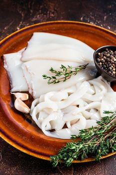 Sliced raw rings squid in a rustic plate with rosemary. Dark background. Top view.