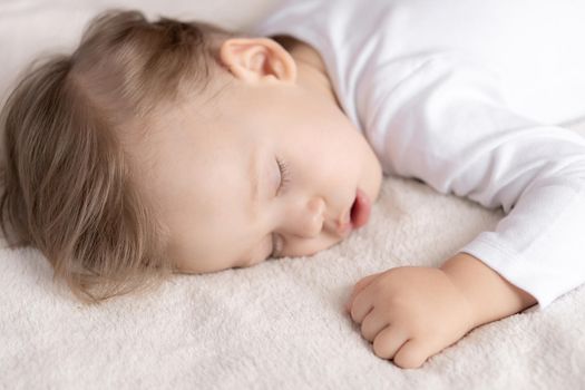 Childhood, sleep, rest, family, lifestyle concept - close-up portrait of a cute little boy of 2 years old in a white body sleeping on a beige bed at noon with mouth open top and side view